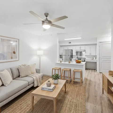 A living room with a grey couch, a wooden table, and a ceiling fan.